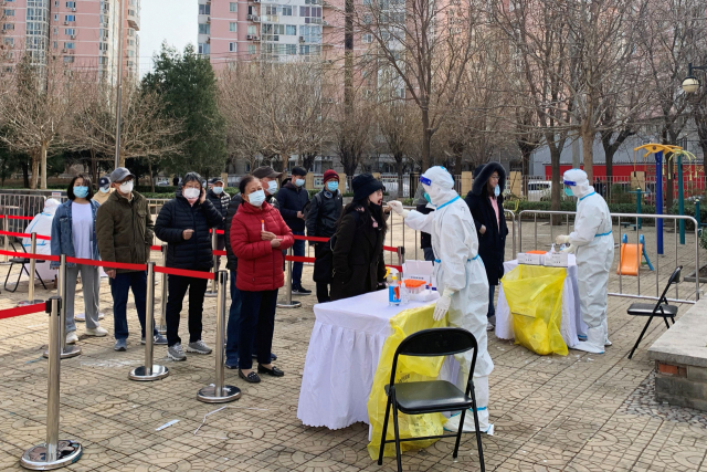 지난 21일(현지시간) 중국 베이징의 한 주택가에 있는 신종 코로나바이러스 감염증(코로나19) 검사장에서 보호복을 입은 근로자가 주민들로부터 검체를 채취하고 있다. 로이터 연합뉴스