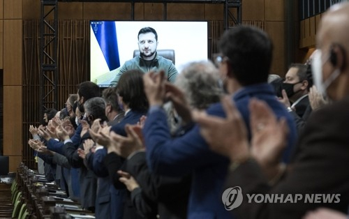 15일(현지시간) 캐나다 수도 오타와의 의사당에서 의원들과 초청 인사들이 대형 모니터 화면에 볼로디미르 젤렌스키 우크라이나 대통령이 화상 연설을 하기 위해 등장하자 기립 박수를 보내고 있다.