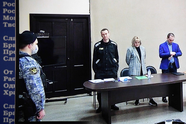 러시아 야권 지도자 알렉세이 나발니(중앙)가 22일(현지시간) 블라디미르주 파크로프의 제2 교도소(IK-2) 내부 법정에서 열린 재판에서 변호사와 함께 기립한 모습이 모니터 화면에 비치고 있다. AFP연합뉴스
