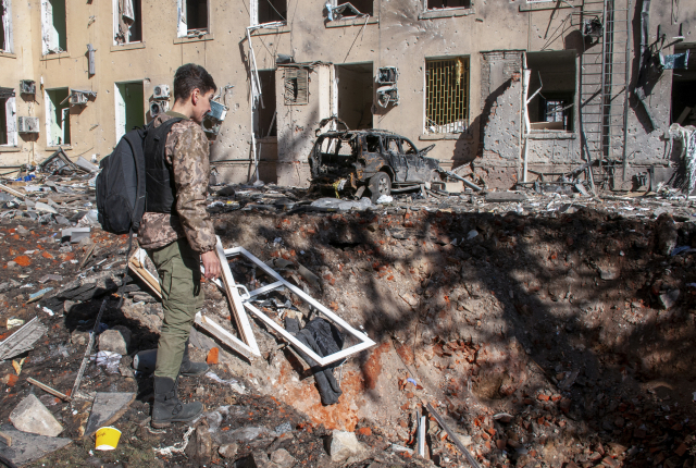 지난 22일(현지시간) 우크라이나 제2 도시인 북동부 하르키우에서 한 남성이 러시아군의 포격으로 시가지에 깊게 파인 포탄 구덩이를 바라보고 있다. EPA 연합뉴스