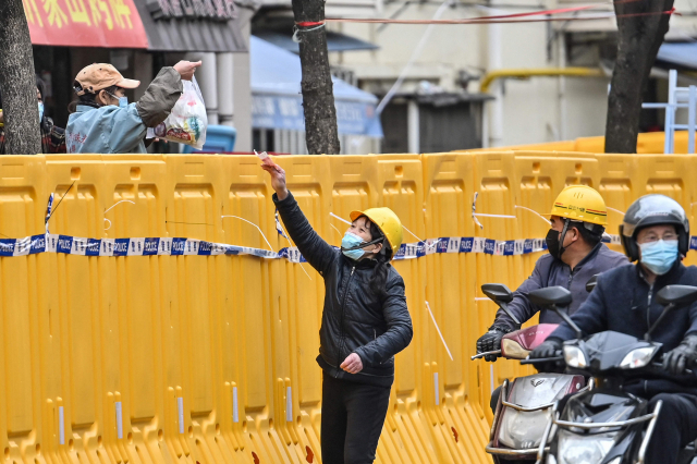 중국 ‘경제 수도’로 꼽히는 상하이에서 31일 코로나 19 확산 방지를 위해 봉쇄된 지역의 여성 상인이 바리케이드 너머로 물건을 팔고 있다. 상하이시는 황푸강을 중심으로 도시를 동서로 나눠 사흘 전부터 순환식 봉쇄를 벌이고 있다. AFP연합뉴스