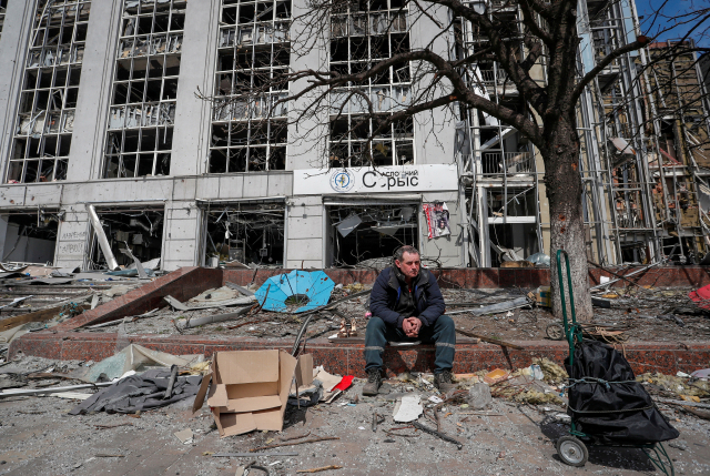 10일(현지시간) 한 주민이 우크라이나 남부 항구도시 마리우폴에서 파괴된 건물 앞에 앉아 있다. 로이터연합뉴스
