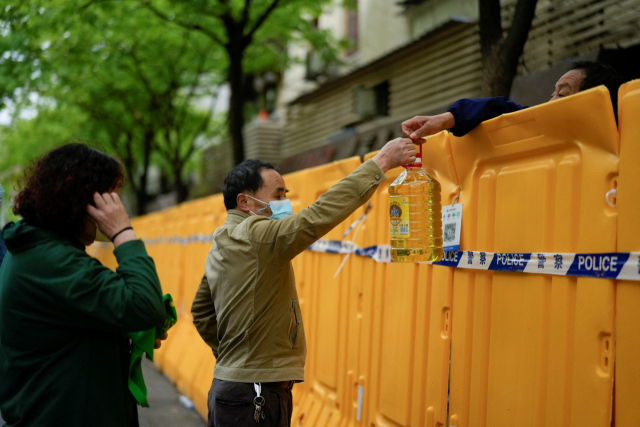 코로나 19 확산 탓에 순환 봉쇄에 들어간 중국 상하이에서 13일 한 시민이 바리케이드 너머로 식용유를 건네 받고 있다. 로이터연합뉴스