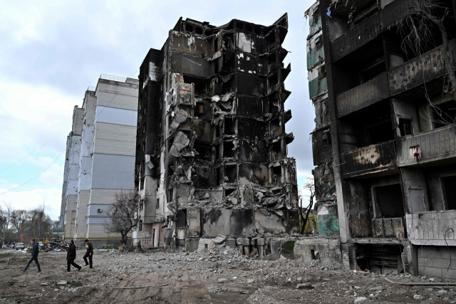 17일(현지시간) 우크라이나 키이우 지역의 한 마을에서 시민들이 폭격으로 파괴된 건물 앞을 걷고 있다. AFP 연합뉴스