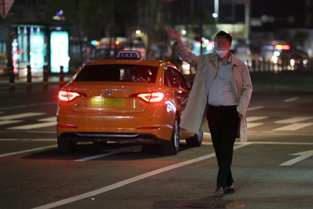 사회적 거리 두기가 전면 해제된 18일 서울 강남역 인근에서 시민이 택시를 잡기 위해 차도에서 손을 들고 있다. 연합뉴스