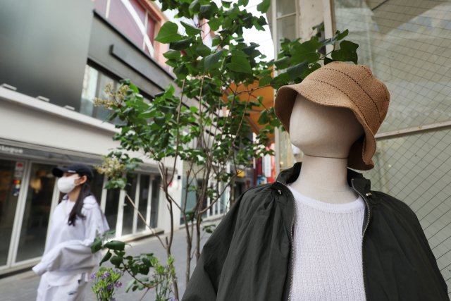 27일 오후 서울 중구 명동거리의 한 옷가게에 놓인 마네킹 뒤로 마스크를 쓴 시민들. 연합뉴스