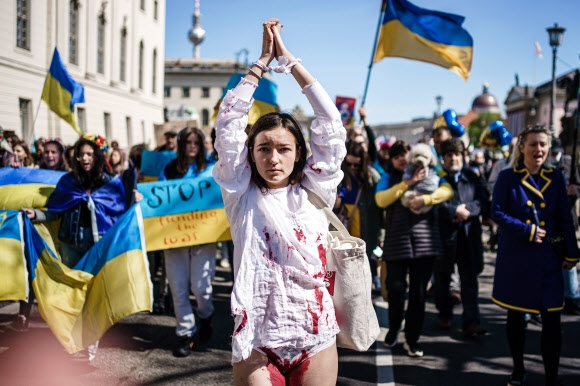 부활절을 맞아 지난달 16일(현지시간) 독일 베를린에서 러시아를 규탄하는 반전 평화시위가 열렸다. 손을 묶고 하얀 옷에 인공 피를 묻힌 한 여성과 함께 “러시아 전쟁을 멈춰라”라고 적힌 플래카드와 우크라이나 국기를 든 참가자들이 행진을 하고 있다. EPA연합뉴스