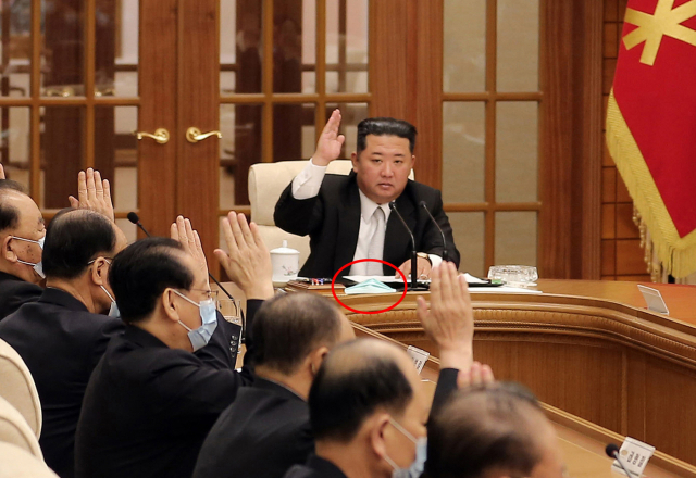 김정은 북한 국무위원장이 12일 당 중앙위원회 제8기 제8차 정치국회의에서 코로나19 확진자 발생 문제를 논의하고 있다. 김 위원장의 책상 앞에는 마스크(빨간 동그라미)가 놓여 있고, 정치국 위원들은 모두 마스크를 착용한 채 회의에 임했다./연합뉴스