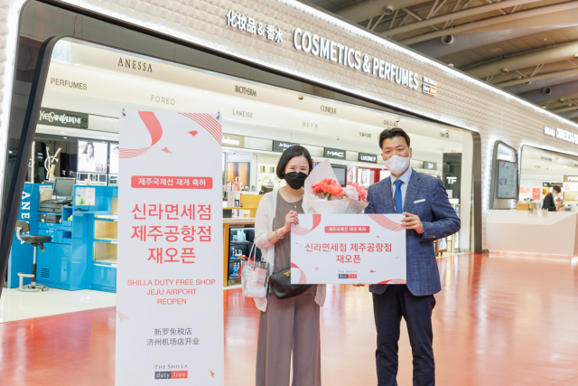 윤재필(오른쪽) 신라면세점 제주공항점장이 2일 저녁 공항점 재 오픈 첫 구매 고객에게 꽃다발과 함께 기념품을 증정하고 기념촬영을 하고 있다./사진제공=신라면세점