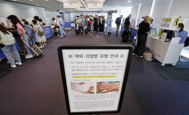 지난달 27일 인천국제공항 제1터미널 입국장에 해외입국자들이 검역을 받기 위해 대기하고 있다. 승객들 앞에는 원숭이두창 관련 안내문이 세워져 있다. 연합뉴스