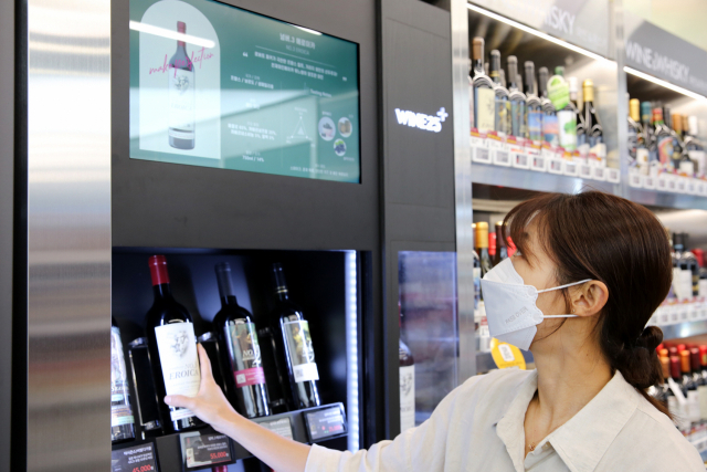 GS25 모델이 서울 강남구 역삼동 GS25 DX LAB점에 설치된 스마트쇼케이스에서 와인을 터치해 상품 설명 디지털 사이니지를 바라보고 있다./사진 제공=GS25