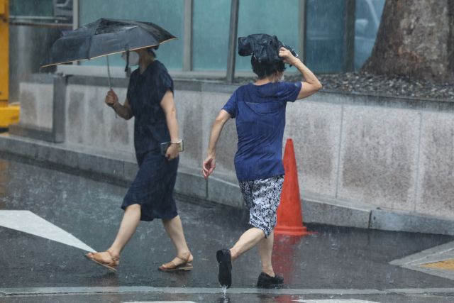 굵은 빗줄기의 소나기가 내린 11일 오후 서울 종로구 세종문화회관 인근에서 우산을 준비하지 못한 시민이 가방을 머리에 올리고 발걸음을 재촉하고 있다. 연합뉴스
