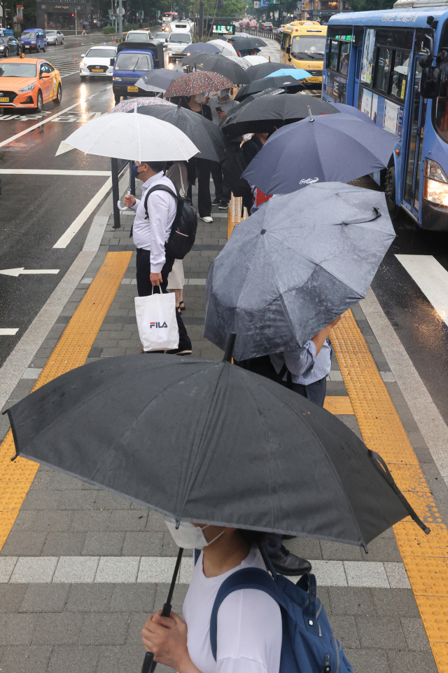 비가 내린 13일 오전 시민들이 서울 종로구 광화문역 인근 교차로에서 우산을 쓰고 신호를 기다리고 있다. 연합뉴스