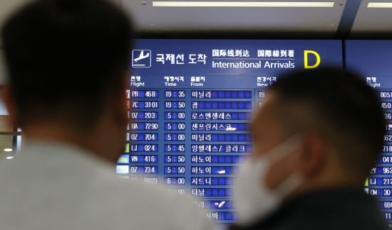 인천국제공항 입국장 전광판에 적혀있는 국제선 도착시간을 보고 있는 승객들의 모습. 연합뉴스
