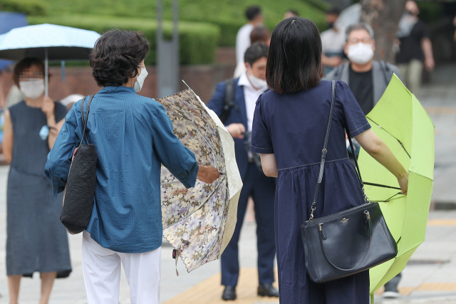 3일 오후 서울 종각역 인근에서 두 시민이 잠시 내린 소나기가 그치자 우산을 접고 있다. 연합뉴스