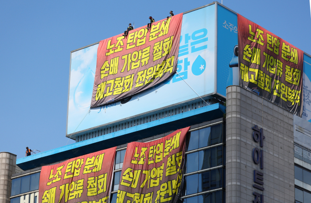 민주노총 공공운수노조 화물연대 소속 조합원들이 16일 서울 강남구 하이트진로 본사 옥상에 설치된 옥외 광고물 위에 올라가 대형 현수막을 내건 채 고공 농성을 벌이고 있다. 이들은 사측에 손해배상 소송과 업무방해 가처분 신청 철회, 해고 조합원 복직, 운송료 현실화 등을 요구하기 위해 이날 오전 6시 10분께 본사를 기습 점거했다. 연합뉴스