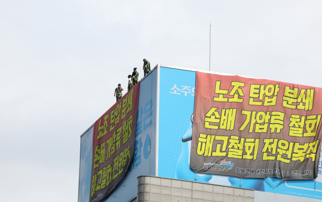 공공운수노조 화물연대가 하이트진로 본사 로비 점거를 해제한 24일 오전 서울 강남구 본사 건물 옥상 농성을 이어가고 있는 조합원들이 로비 점거를 해제하고 건물을 나선 다른 조합원들을 바라보고 있다. 연합뉴스