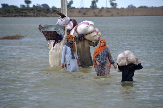 24일(현지시간) 파키스탄 남서부 발루치스탄주 자프라바드에서 한 이재민 가족이 가재도구 등을 짊어지고 폭우로 침수된 지역을 지나고 있다. AP연합뉴스