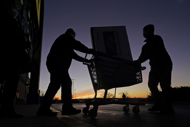 FILE - People transport a television to their car after shopping at a Best Buy store, Nov. 26, 2021, in Overland Park, Kan. A stronger dollar helps U.S. shoppers by keeping a lid on prices for imports and pushing downward on inflation. (AP Photo/Charlie Riedel, File) FILE