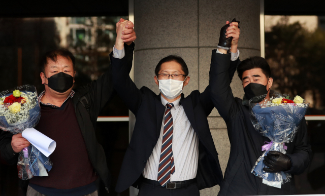 경찰 고문과 가혹행위로 인해 살인죄 누명을 쓴 채 21년간 억울한 옥살이를 한 '낙동강변 살인사건' 피해 당사자 최인철(사진 왼쪽)씨와 장동익씨(사진 오른쪽), 박준영 변호사가 지난해 2월4일 부산고등법원에서 열린 재심 선고 공판을 마치고 손을 맞잡고 있다. 부산고법 제1형사부는 이날 재심청구 선고 재판에서 두 사람에게 무죄를 선고했다. 연합뉴스