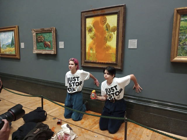 14일(현지시간) 영국의 환경단체 ‘저스트 스톱 오일’ 소속 활동가 2명이 런던 내셔널 갤러리에서 빈센트 반 고흐의 그림 ‘해바라기’에 토마토 수프를 뿌리고 난 뒤 자신들의 손을 미술관 벽에 붙이고 있다. AP연합뉴스
