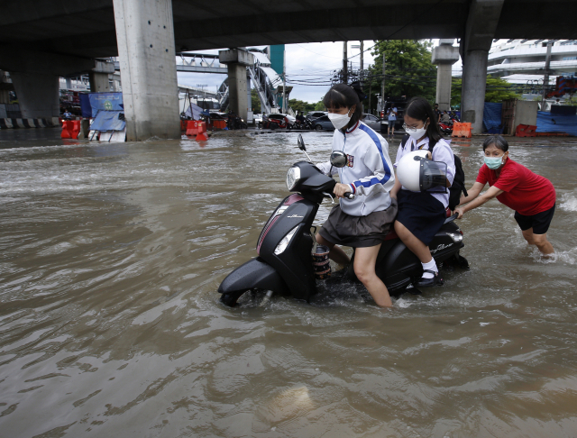 지난 9월 폭우로 차오프라야강이 범람한 영향으로 도시가 침수된 태국 수도 방콕에서 한 여성이 학생들이 올라 탄 오토바이를 밀고 있다. EPA연합뉴스