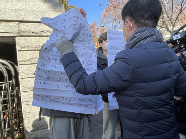 15일 대구 북구 대현동 경북대 서문에서 경북대 재학생과 졸업색 2명이 '돼지고기 바비큐' 행사를 비판하는 대자보를 들어 보이자 일부 대현동 주민들이 항의하고 있다. 연합뉴스