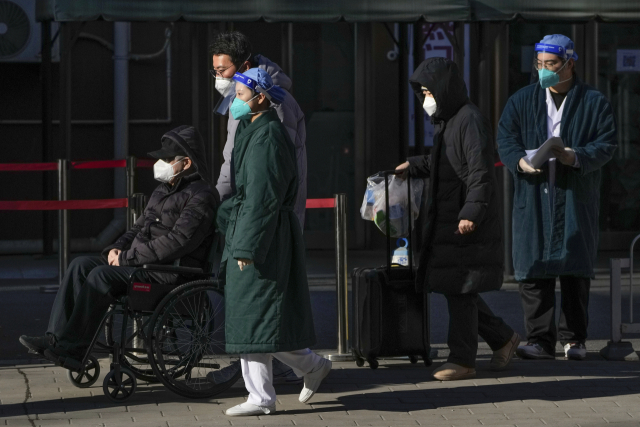 보호장비를 착용한 의료진이 19일 베이징의 한 병원에서 발열 클리닉을 나서는 노인 환자를 휠체어에 태운 가족들과 함께 지나가고 있다. AP연합