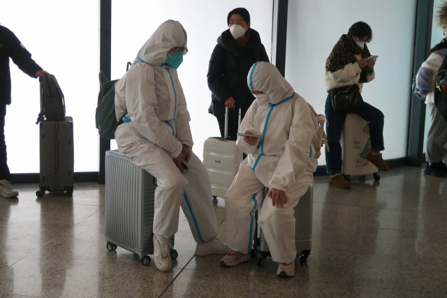 지난해 12월 중국 후베이성 우한의 한 기차역 대기실에 방역복을 입은 사람들이 여행용 트렁크에 앉아 기다리고 있다. 연합뉴스