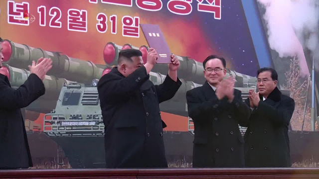 김정은(왼쪽) 북한 국무위원장은 지난달 31일 노동당에 증정된 자칭 초대형 방사포(KN-25, 배경 그림)의 ‘증정서’를 들어보이고 있다. 조선중앙TV·연합뉴스