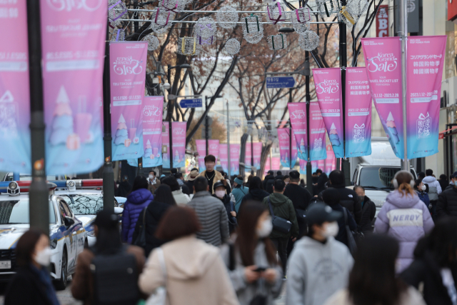 12일 ‘2023 코리아그랜드세일’을 알리는 플래카드가 나부끼는 서울 명동 거리를 관광객들이 지나고 있다. 연합뉴스