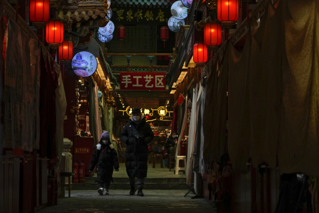 베이징의 유명 관광지인 첸먼에서 3일 기념품을 파는 폐쇄된 상점 옆을 마스크를 쓴 한 남자와 아이가 걷고 있다. AP연합.