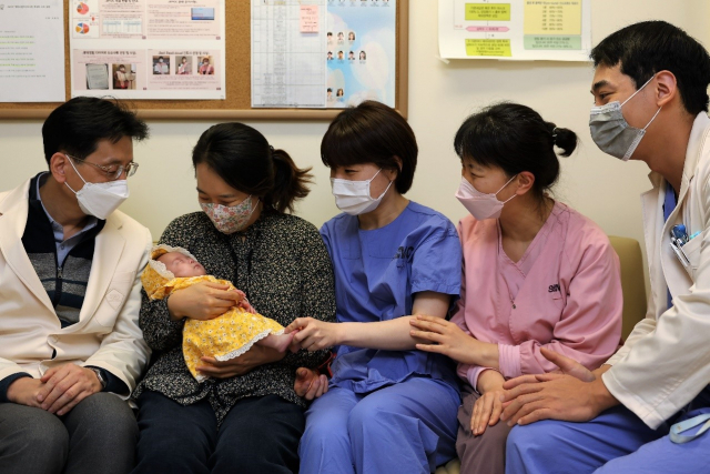 송진영(왼쪽) 삼성서울병원 소아청소년과 교수와 윤슬이를 안고 있는 엄마 김노을(왼쪽 두번째)씨가 의료진들과 함께 윤슬이의 퇴원을 앞두고 기념 사진을 촬영하고 있다. 사진 제공=삼성서울병원