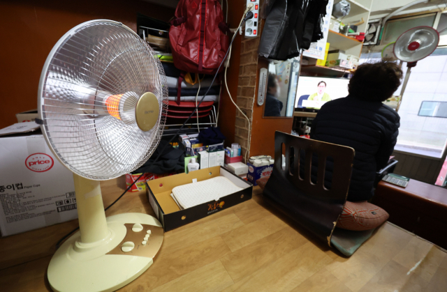 지난 1일 서울 중구의 한 가게에서 상인이 전기난로로 추위를 피하고 있다. 연합뉴스