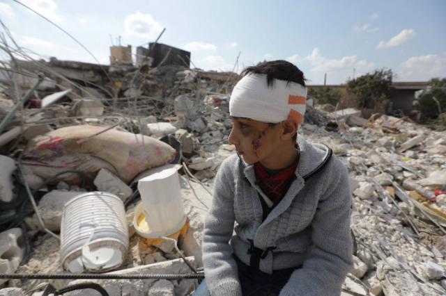 11일(현지시간) 시리아 알레포주 진데리스에서 한 소년이 머리에 붕대를 감은 채 지진으로 붕괴한 건물 잔해 더미에 앉아 있다. 이 소년은 시리아와 인접한 튀르키예 남동부에서 지난 6일 발생한 강진으로 가족을 잃었다. 연합뉴스 캡처