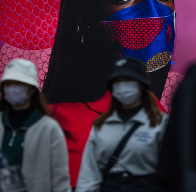 지난 15일 서울 명동의 마스크 전문 상점의 간판 앞을 마스크를 쓴 시민과 관광객이 지나가고 있다. 연합뉴스