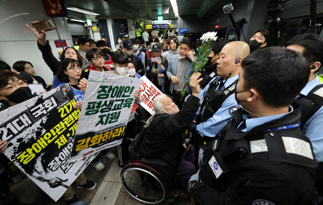 박경석 전국장애인차별철폐연대(전장연) 대표가 지난 21일 오전 서울 지하철 5호선 광화문역에서 탑승 시위 중 지하철 탑승을 저지 당하자 국화꽃을 던지고 있다. 연합뉴스