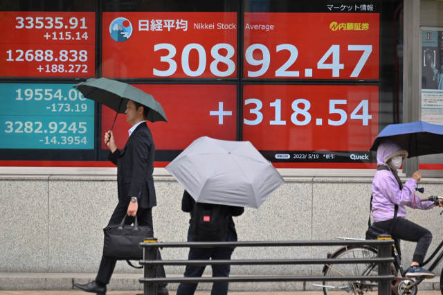 19일 일본 도쿄에서 시민들이 닛케이225지수가 3만 800선을 넘었다는 것을 보여주는 전광판 앞을 지나가고 있다. AFP연합뉴스