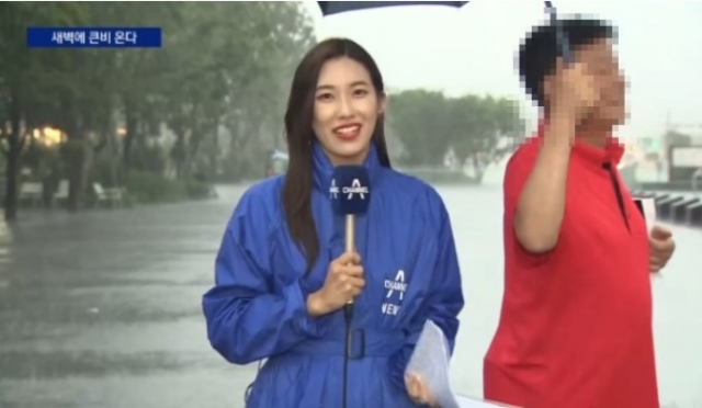 비를 맞으며 보도를 하고 있는 기자에게 한 남성이 우산을 씌워주고 있다. 사진=채널A뉴스 캡처