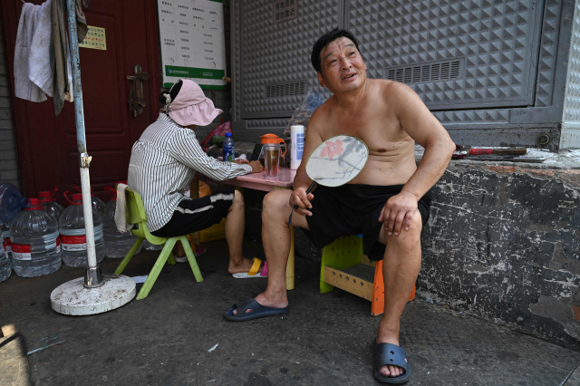중국 베이징에서 섭씨 40도를 넘는 기록적 폭염이 이어지는 가운데 19일 한 시민이 골목에 앉아 부채질을 하며 더위를 식히고 있다. 중국 정부는 폭염이 예정된 날은 외부 활동 자제를 권고하고 있다. AFP연합뉴스
