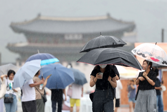 서울 전역에 호우주의보가 발효된 23일 오전 광화문광장에서 시민들이 우산을 쓴 채 걸어가고 있다. 연합뉴스