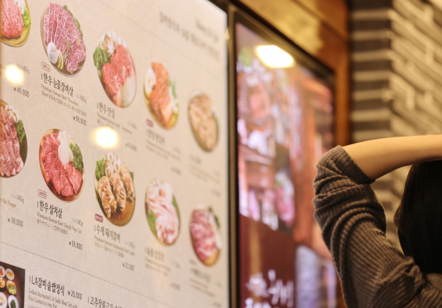지난 17일 서울 명동의 한 식당 메뉴판 앞에서 시민이 머리를 감싸쥐고 있다. 사진. 연합뉴스