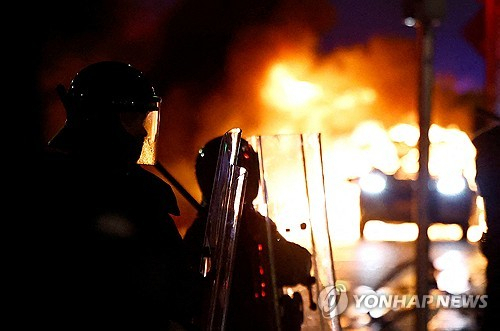 23일(현지시간) 아일랜드 더블린 시내에서 경찰관들이 불타는 경찰 차량을 바라보고 있다. 로이터·연합뉴스