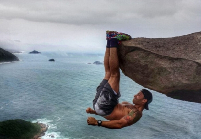 브라질의 보디빌더 루이스 페르난도 칸델라가 300m 높이 해안 절벽에 거꾸로 매달려 아찔한 상황을 연출하고 있다. 사진=데일리메일 캡쳐