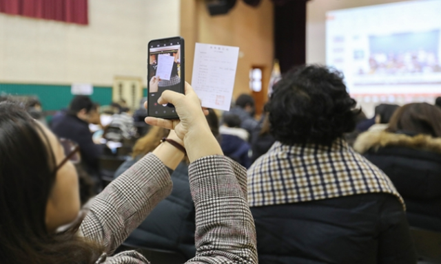 초등학교 신입생 예비소집에 참석한 한 학부모가 설명회장을 배경으로 취학통지서를 스마트폰으로 찍고 있다. 연합뉴스