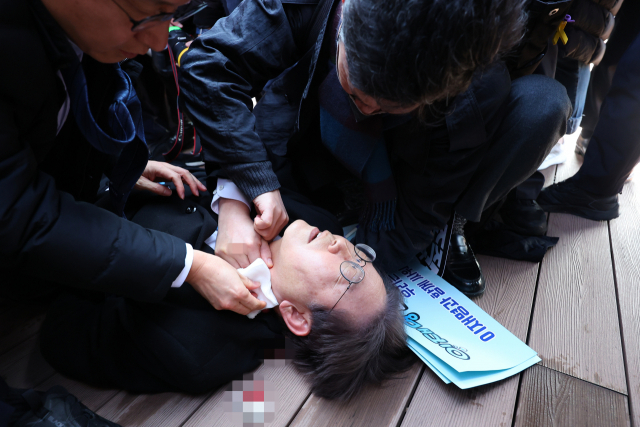 이재명 더불어민주당 대표가 2일 부산 가덕도 신공항 부지를 둘러본 후 기자들과 문답을 진행하던 중 왼쪽 목 부위에 습격을 당해 피를 흘린 채 쓰러져 있다. 연합뉴스