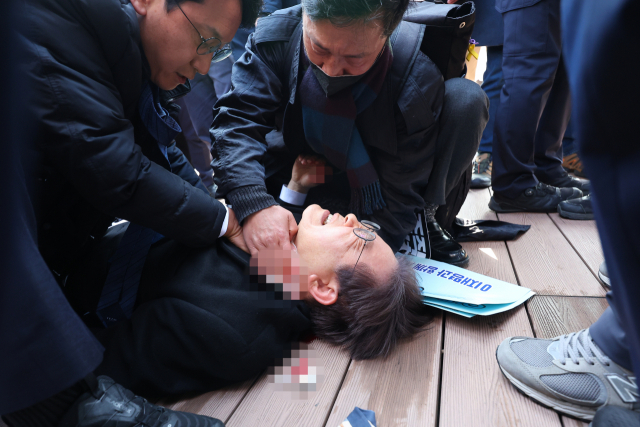 더불어민주당 이재명 대표가 2일 부산 가덕도 신공항 부지를 둘러본 후 기자들과 문답을 진행하던 중 왼쪽 목 부위에 습격을 당해 피를 흘린 채 쓰러져 있다.연합뉴스