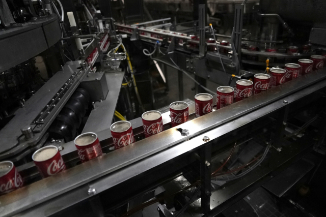 File - Coca-Cola cans move down a conveyer belt in the Swire Coca-Cola bottling plant on Oct. 20, 2023, in Denver. On Thursday, the government issues the first of three estimates of GDP growth in the United States during the October-December quarter. (AP Photo/Brittany Peterson, File) FILE