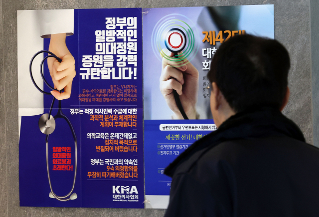 지난 12일 한 시민이 서울 용산구 대한의사협회 건물에서 정부의 의대정원에 반대하는 포스터를 바라보고 있다. 성형주기자