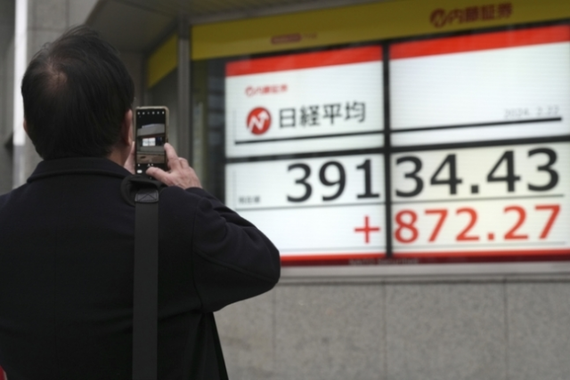 22일 일본 도쿄 시내에서 한 행인이 증시 현황판을 휴대폰으로 찍고 있다. AP연합뉴스